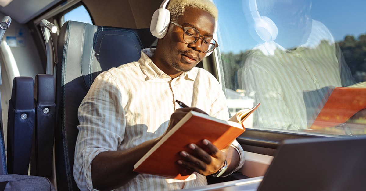 man writing in a notebook while seated on a train